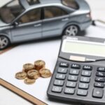 Calculadora, moedas e carro em miniatura sobre prancheta