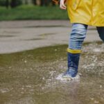 Criança de capa de chuva e botas em poça de chuva