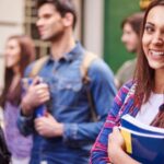 Estudante sorrindo segurando livros rodeada por outros estudantes