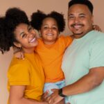 Família de três pessoas posando e sorrindo para foto em fundo marrom