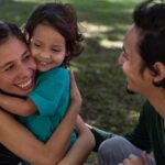 Família de três pessoas sorrindo em ambiente verde