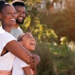 Família de três pessoas sorrindo em fundo com vegetação