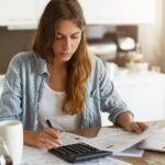 Mulher em cozinha com notebook, contas e calculadora