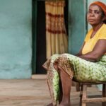Mulher negra sentada em banco do lado de fora de casa