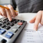 Pessoa com lápis de escrever, calculadora e tabela de preços