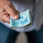 Pessoa de jeans segurando notas de cem