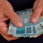 Pessoa de preto contando notas de cem e cinquenta
