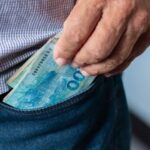Pessoa guardando notas de dinheiro no bolso da calça jeans