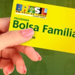 Pessoa segurando o cartão Bolsa Família em fundo verde