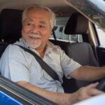 Senhor grisalho dirigindo carro azul