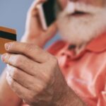 Senhor grisalho falando ao telefone e segurando cartão