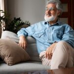 Senhor grisalho olhando pela janela sentado em sofá