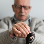 Zoom em mãos de senhor se apoiando em bengala