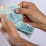Zoom em pessoa contando notas de cinquenta e cem reais