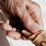 Zoom em pessoa idosa segurando nota de cinquenta reais enrolada
