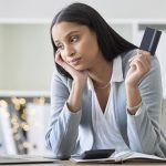 mulher com cartão olhando pensativa para notebook