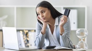 mulher com cartão olhando pensativa para notebook